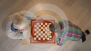 Grandfather and grandson plays chess. Elderly man teaches chess to play a young fat child. Home comfort, family idyll