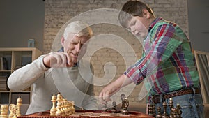 Grandfather and grandson are preparing to play chess. An elderly man teaches a fat child how to play chess. Expose the