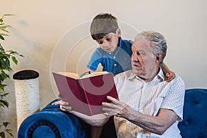 Grandfather and grandson read a book while sitting on the sofa