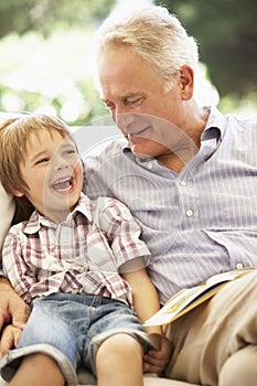 Grandfather With Grandson Reading Together On Sofa