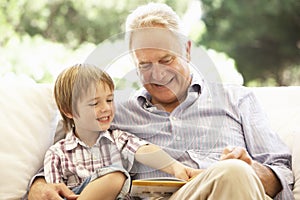 Grandfather With Grandson Reading Together On Sofa