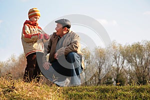 Grandfather and the grandson sit on hillock photo