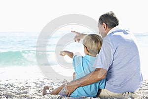 Grandfather And Grandson Sitting On Beach Together On Holiday