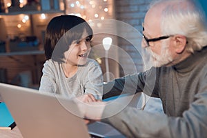 Grandfather and grandson sitting on laptop at night at home.