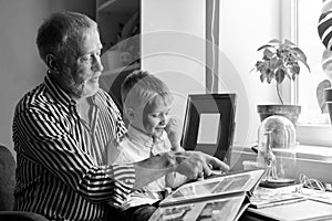 Grandfather and grandson on sofa at home. Grandpa and children watching old photos