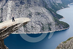 Grandfather and grandson standing on Trolltunga rock formation and waving hands. Jutting cliff is in Odda, Hordaland county,