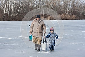 Grandfather and grandson are walking along the icebound river for winter fishing