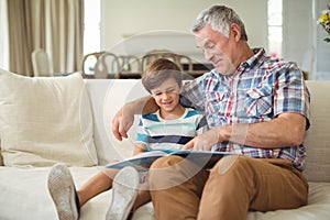 Grandfather with her grandson reading book on sofa