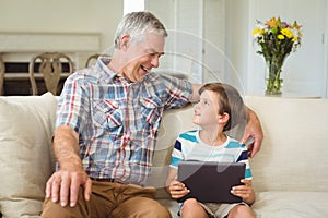 Grandfather with her grandson using digital tablet on sofa