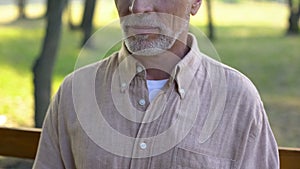 Grandfather in his 60s sitting on bench, retirement tranquility in countryside