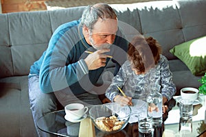 Grandfather and his grandson spending time insulated at home, stadying, writing, drawing or playing together