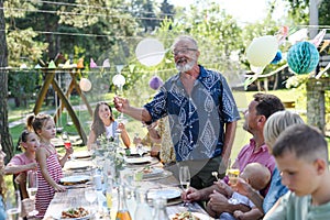 Grandfather holding champagne glass. Senior man making celebratory toast at outdoor summer garden party.