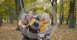 Grandfather holding granddaughter piggyback in autumn park