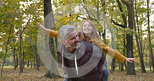 Grandfather holding granddaughter piggyback in autumn park