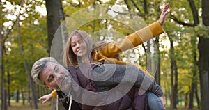 Grandfather holding granddaughter piggyback in autumn park