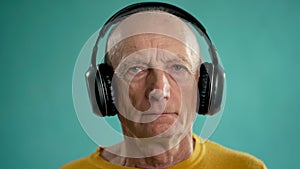 Grandfather listening to music with headphones on a blue background. Pensioners concept