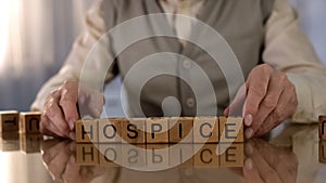 Grandfather making word hospice of wooden cubes on table, elder care, disorder