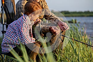 Grandfather mentoring grandson to fish at young age, side view, in nature, countryside