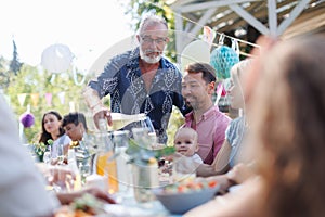 Grandfather opening bottle of champagne, pouring wine into glasses. Senior man making celebratory toast at outdoor