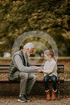 Grandfather playing red hands slapping game with his granddaughter in park on autumn day