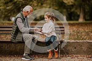 Grandfather playing red hands slapping game with his granddaughter in park on autumn day