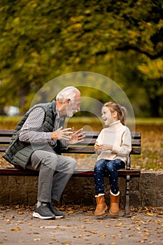 Grandfather playing red hands slapping game with his granddaughter in park on autumn day