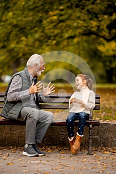 Grandfather playing red hands slapping game with his granddaughter in park on autumn day