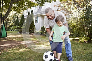 Grandfather Playing Soccer In Garden With Grandson