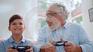 Grandfather playing video game with grandson. Mature man and boy using joysticks
