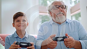 Grandfather playing video game with grandson. Mature man and boy using joysticks