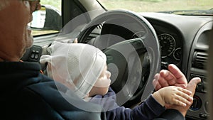 Grandfather plays with the boy in the car while driving. The grandson is very happy and twists the different buttons
