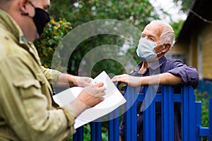 Grandfather in protective mask talking to census agent standing at fence of his country house