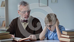 Grandfather reading aloud book, little boy looks bored, generation gap problem