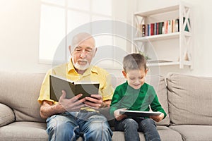 Grandfather reading book, grandson using tablet