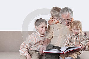 Grandfather reading an interesting book for his three grandchildren