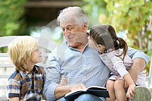 Grandfather reading story to grandchildren in the garden