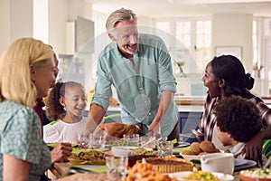 Grandfather Serving As Multi-Generation Family Celebrating Thanksgiving At Home Eating Meal Together