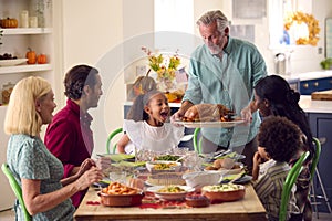 Grandfather Serving As Multi-Generation Family Celebrating Thanksgiving At Home Eating Meal Together