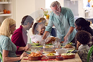 Grandfather Serving As Multi-Generation Family Celebrating Thanksgiving At Home Eating Meal Together