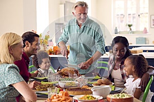 Grandfather Serving As Multi-Generation Family Celebrating Thanksgiving At Home Eating Meal Together