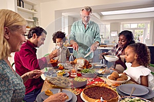 Grandfather Serving As Multi-Generation Family Celebrating Thanksgiving At Home Eating Meal Together