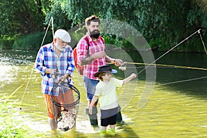 Grandfather with son and grandson having fun in river. Summer day. Grandfather, father and son are fly fishing on river.