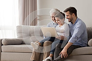 Grandfather son and grandson using laptop sitting on couch indoors