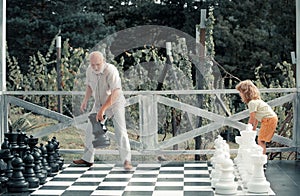 Grandfather and son playing chess on big chess board. Weekend with granddad.