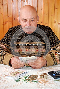 The grandfather in a sweater sits at the dacha at a table and counts money.