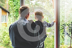 Grandfather taking care and spending time together with grandson at home. looking through the window