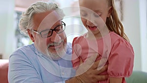 Grandfather talking with granddaughter at home. Girl sitting on grandfather laps