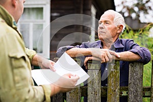 Grandfather talking to census agent standing at fence of his country house