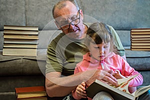 Grandfather teaches his granddaughter to read books. Family educational concept. An elderly man and a little girl leaf through a