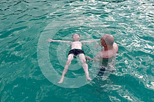 Grandfather teaches his grandson to swim on his back in pool